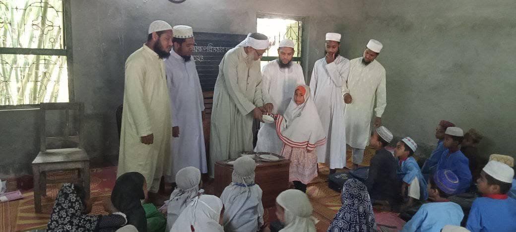 A girl receiving her prize from a teacher as classmates look on